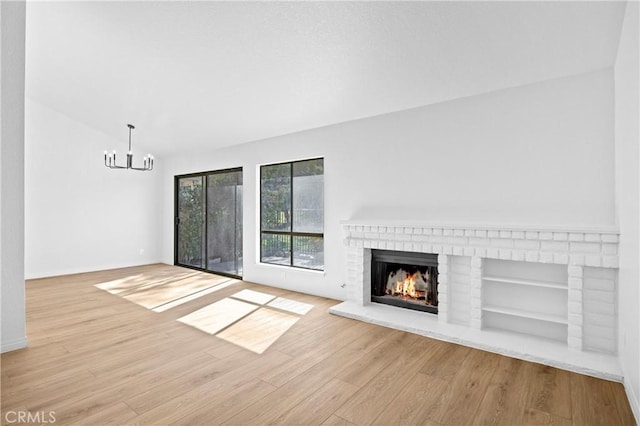 unfurnished living room with baseboards, lofted ceiling, wood finished floors, a brick fireplace, and a chandelier