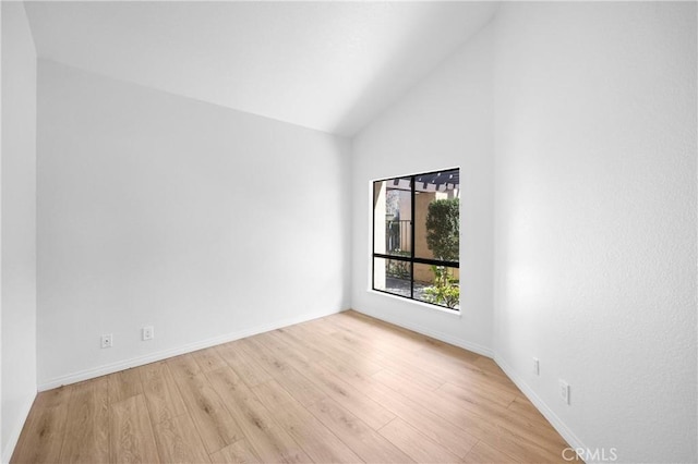 empty room with high vaulted ceiling, light wood finished floors, and baseboards