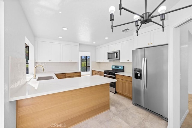 kitchen featuring white cabinets, a peninsula, stainless steel appliances, light countertops, and a sink