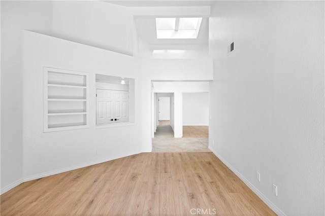 empty room with built in shelves, a high ceiling, wood finished floors, visible vents, and baseboards