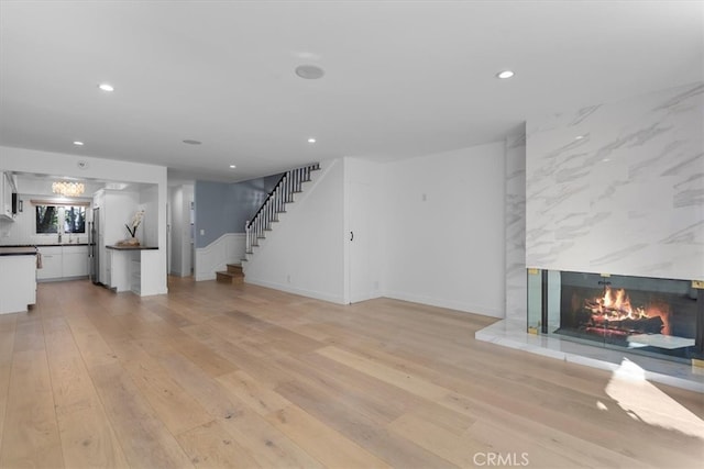 unfurnished living room with stairs, recessed lighting, light wood finished floors, and a premium fireplace