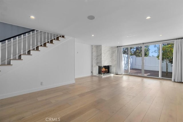 unfurnished living room featuring stairs, recessed lighting, wood finished floors, and a premium fireplace