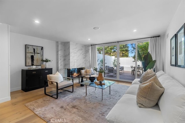 living room featuring baseboards, a premium fireplace, light wood-type flooring, and recessed lighting
