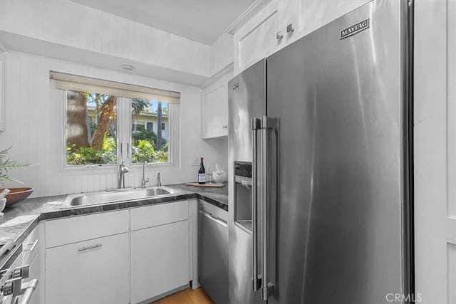 kitchen with dark countertops, a sink, white cabinetry, and appliances with stainless steel finishes