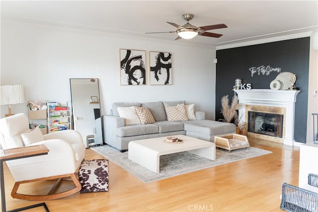 living room featuring a premium fireplace, crown molding, ceiling fan, and wood-type flooring