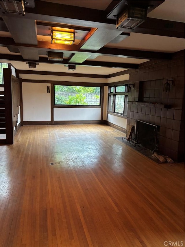 unfurnished living room with beamed ceiling, a tiled fireplace, and light hardwood / wood-style flooring