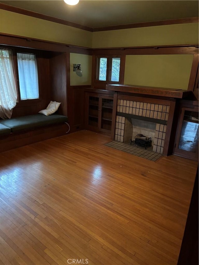 unfurnished living room with a tiled fireplace, crown molding, a wealth of natural light, and light hardwood / wood-style flooring