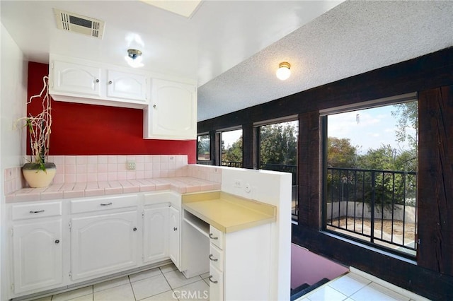 kitchen with tile counters, light tile patterned floors, a textured ceiling, and white cabinets