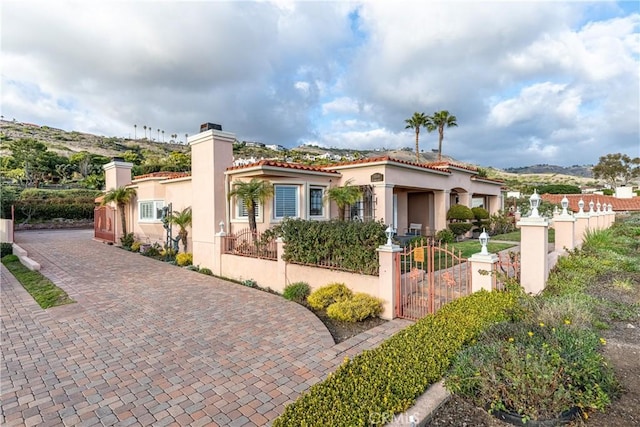 mediterranean / spanish house with a fenced front yard, a chimney, a tiled roof, a gate, and stucco siding