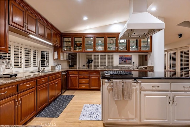 kitchen with dark stone counters, a sink, glass insert cabinets, and island range hood