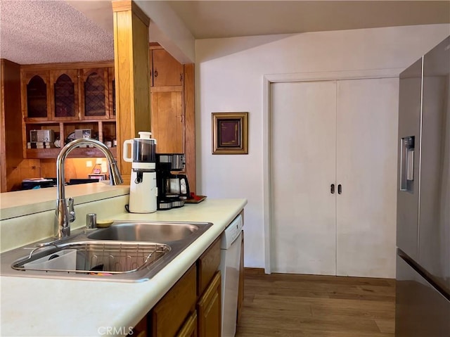 kitchen featuring sink, stainless steel fridge, white dishwasher, light hardwood / wood-style floors, and a textured ceiling