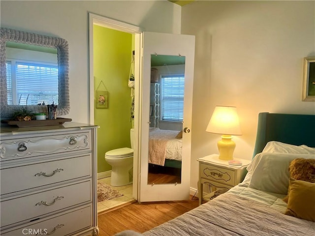 bedroom featuring ensuite bath, multiple windows, and light wood-type flooring