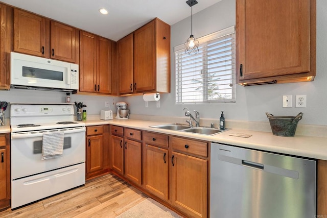 kitchen featuring hanging light fixtures, sink, white appliances, and light wood-type flooring