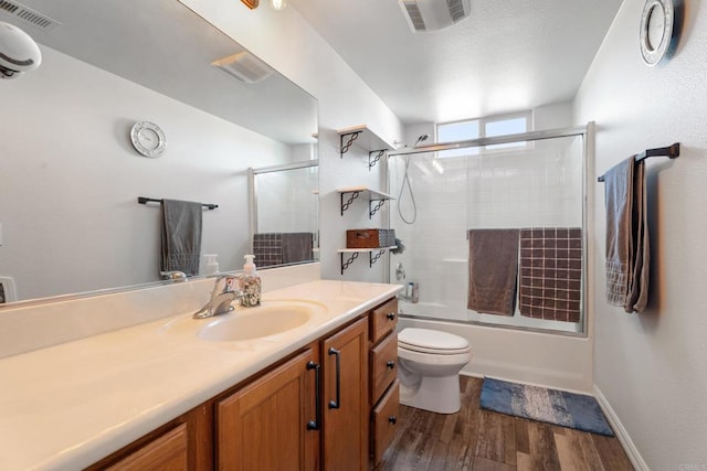 full bathroom featuring hardwood / wood-style flooring, vanity, combined bath / shower with glass door, and toilet