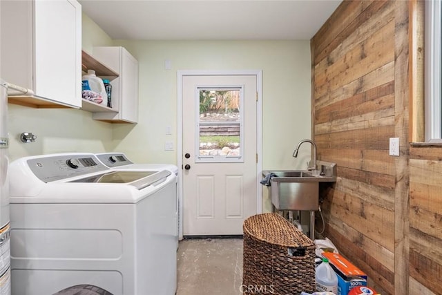 clothes washing area featuring cabinets, sink, washing machine and dryer, and wood walls