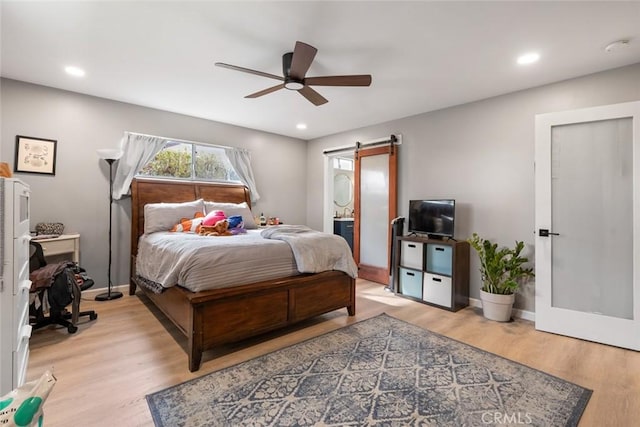 bedroom with light hardwood / wood-style floors, a barn door, and ceiling fan