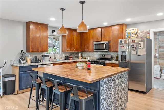 kitchen with pendant lighting, sink, a breakfast bar area, stainless steel appliances, and light wood-type flooring