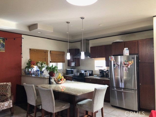 kitchen with light tile patterned flooring, a kitchen bar, appliances with stainless steel finishes, pendant lighting, and wall chimney range hood