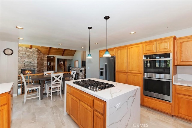 kitchen with hanging light fixtures, stainless steel appliances, light stone countertops, a kitchen island, and a stone fireplace