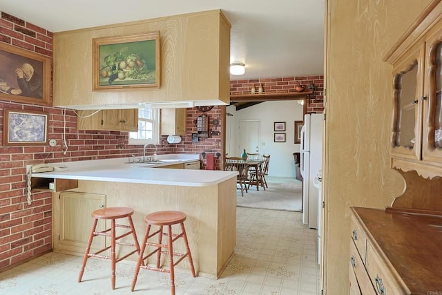 kitchen with sink, a kitchen bar, brick wall, light brown cabinetry, and kitchen peninsula