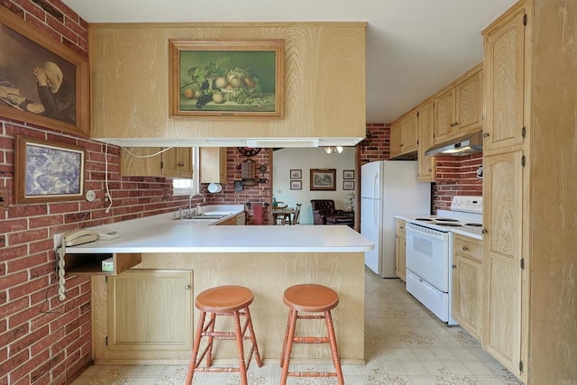 kitchen featuring brick wall, sink, a kitchen breakfast bar, kitchen peninsula, and white appliances