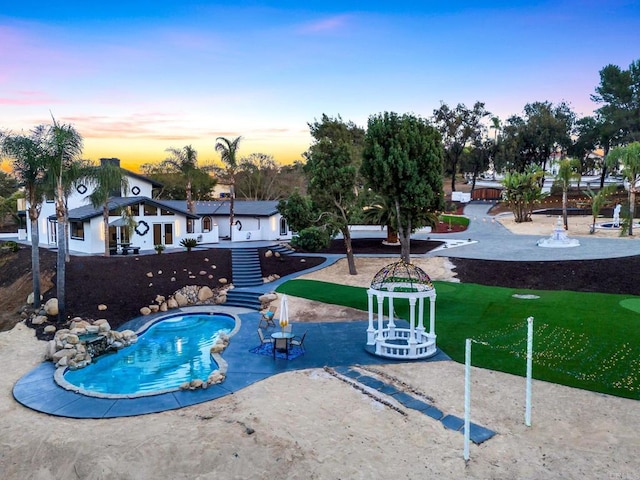 pool at dusk featuring a patio area and a lawn