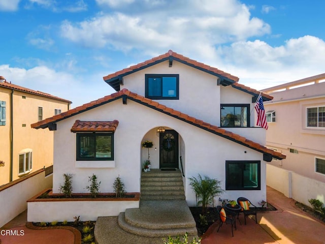 mediterranean / spanish-style home with a tiled roof, a patio area, fence, and stucco siding