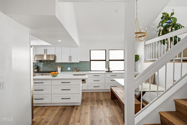 kitchen featuring white cabinets, light wood-style floors, light countertops, under cabinet range hood, and pendant lighting