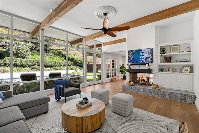 living room with a fireplace, beamed ceiling, light wood-type flooring, and a wall of windows