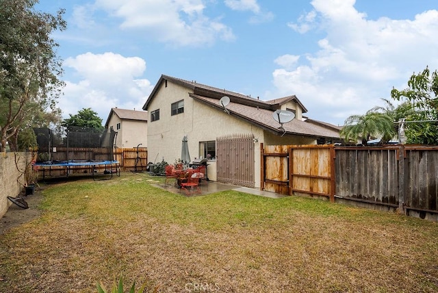 rear view of house with a trampoline, a lawn, and a patio