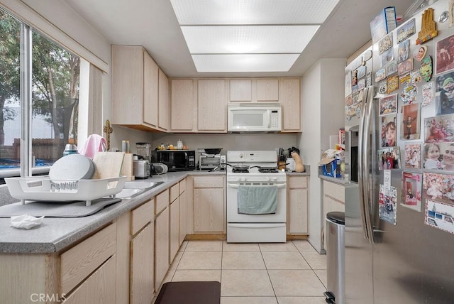 kitchen with light tile patterned flooring, white appliances, and light brown cabinets