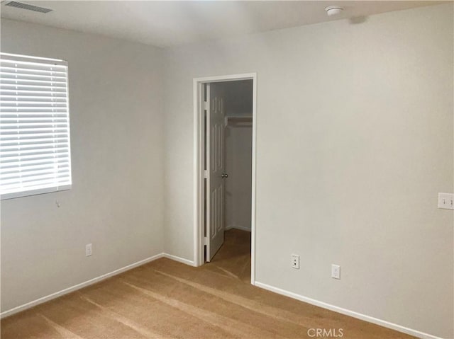 unfurnished bedroom with visible vents, a closet, baseboards, a walk in closet, and light colored carpet