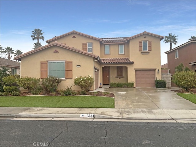 mediterranean / spanish home featuring a tiled roof, an attached garage, concrete driveway, and stucco siding