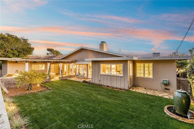 back of house at dusk with a patio area, stucco siding, board and batten siding, and a yard