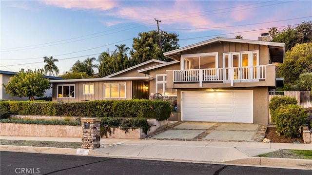 split level home featuring a balcony, stucco siding, concrete driveway, a garage, and board and batten siding