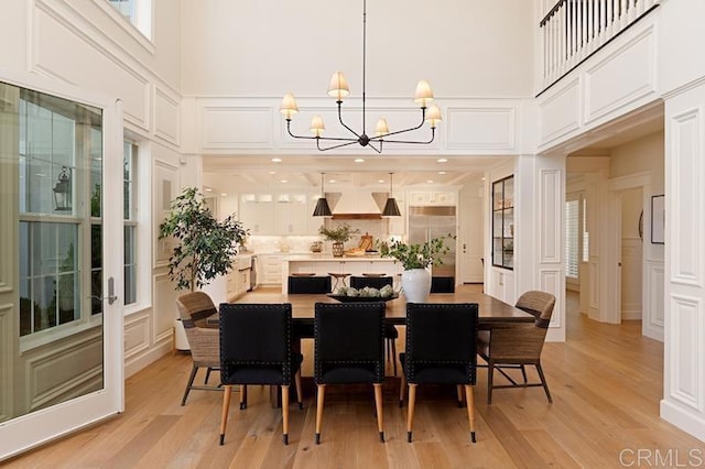 dining room featuring light wood-style floors, a notable chandelier, a decorative wall, and a high ceiling