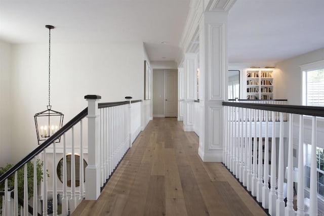 hall with wood finished floors, an upstairs landing, and an inviting chandelier