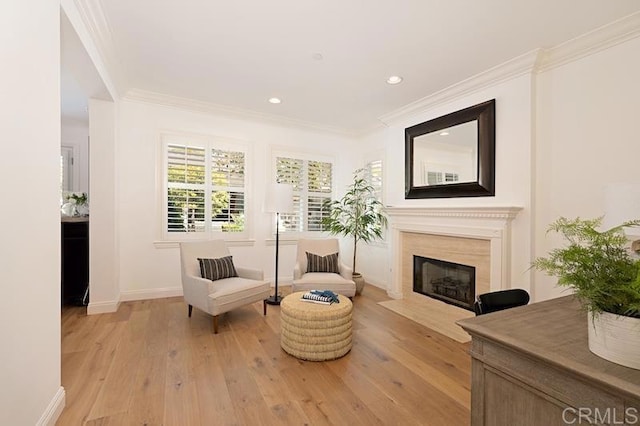 living area featuring ornamental molding, baseboards, light wood-style flooring, and a fireplace with flush hearth