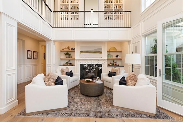 living room with built in features, a decorative wall, a towering ceiling, and wood finished floors