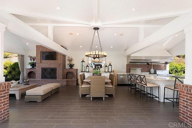 dining area featuring wood finish floors, recessed lighting, lofted ceiling with beams, an inviting chandelier, and an outdoor brick fireplace