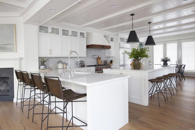 kitchen featuring a breakfast bar area, custom exhaust hood, light countertops, glass insert cabinets, and white cabinets