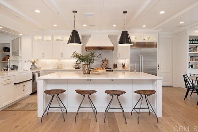 kitchen with a center island with sink, custom range hood, glass insert cabinets, appliances with stainless steel finishes, and light countertops