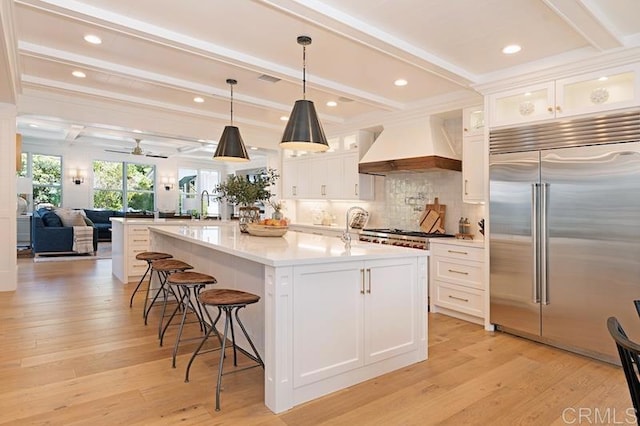 kitchen featuring glass insert cabinets, custom range hood, appliances with stainless steel finishes, and light countertops