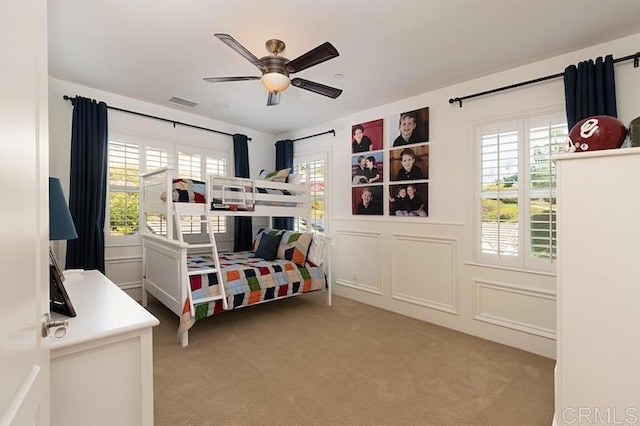 bedroom featuring light carpet, ceiling fan, visible vents, and a decorative wall