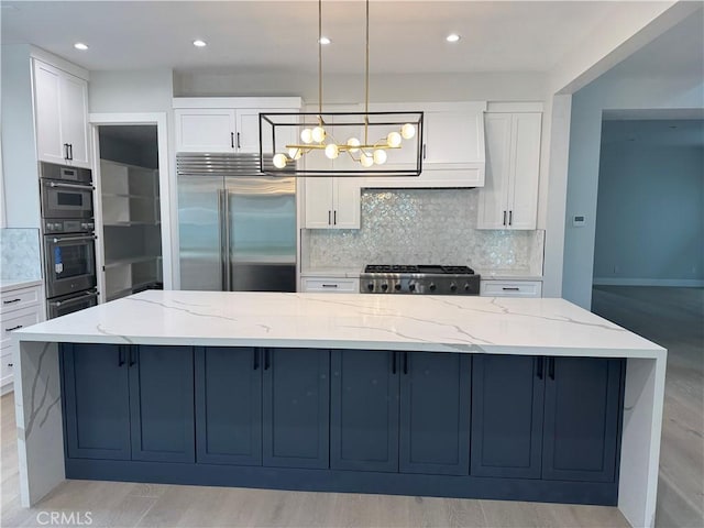 kitchen with pendant lighting, a spacious island, light stone countertops, white cabinets, and built in fridge