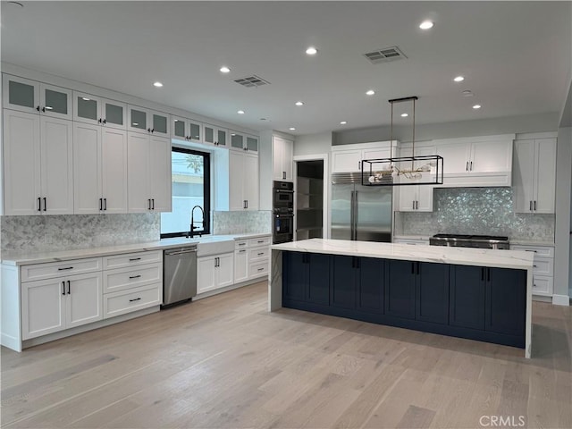 kitchen with pendant lighting, appliances with stainless steel finishes, a spacious island, light stone countertops, and white cabinets