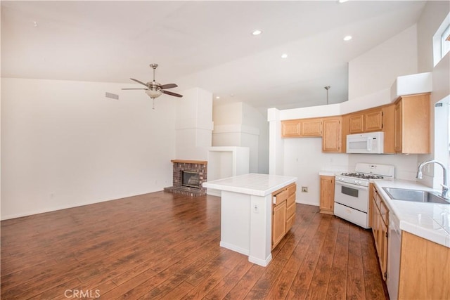 kitchen with sink, a brick fireplace, dark hardwood / wood-style flooring, a kitchen island, and white appliances