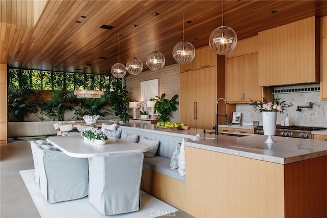 kitchen with tasteful backsplash, sink, pendant lighting, and a kitchen island with sink