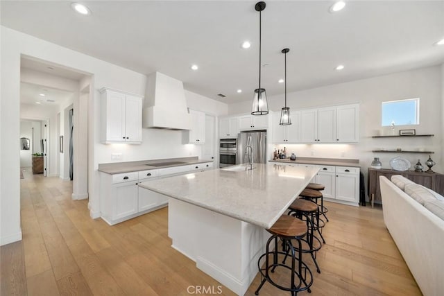 kitchen with premium range hood, stainless steel appliances, an island with sink, and white cabinets
