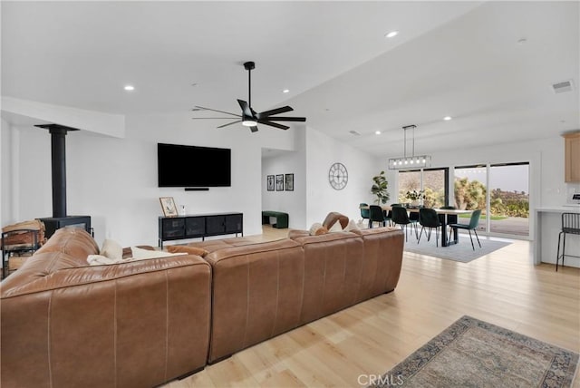 living room featuring ceiling fan, vaulted ceiling, a wood stove, and light hardwood / wood-style floors